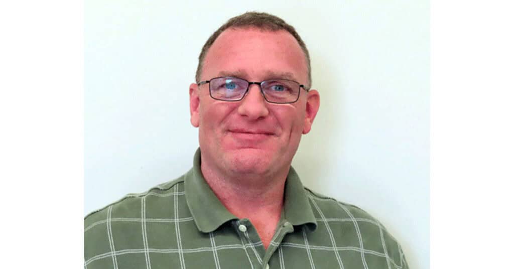 Male professional wearing glasses and a green checkered polo shirt, smiling against a plain white background, representing Perimeter's expertise in network security solutions.