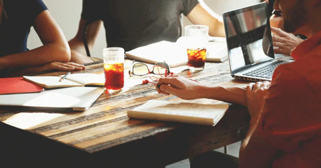 Remote team meeting with laptops, notebooks, and drinks on a rustic wooden table, promoting collaboration, productivity, and effective communication in a modern workspace.