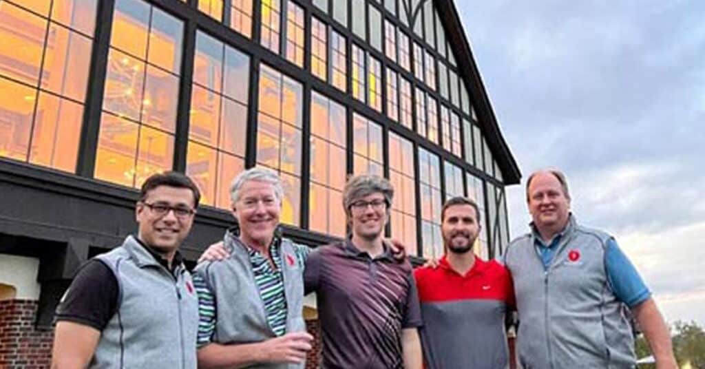 Group of five professionals outside an office building during daytime, showcasing teamwork and corporate collaboration. The modern glass architecture in the background highlights innovation and business success.