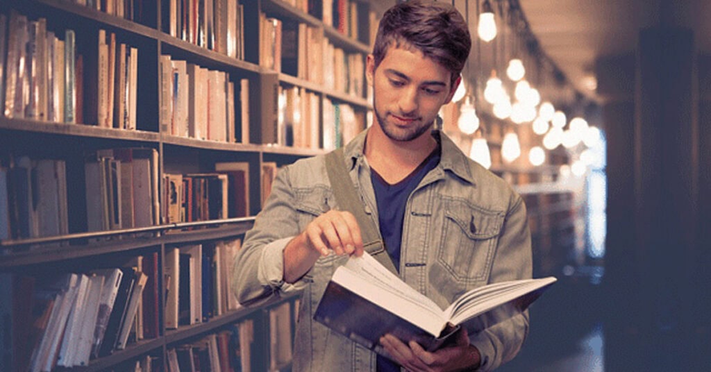 A young man reading a book in a modern library with warm lighting and extensive bookshelves, creating an inviting atmosphere for learning and exploration.